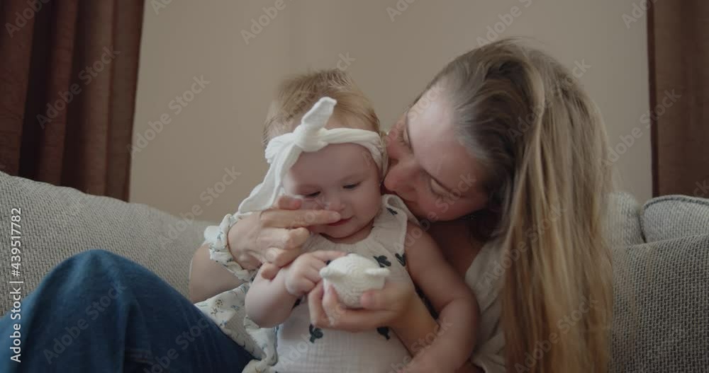 Mother and daughter spend time at home together. Young mom plays with her adorable little child on a sofa in the leaving room. Mother and daughter spend time at home together. Young mom plays with her adorable little child on a sofa in the leaving room.