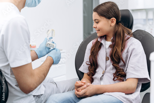 Dentist communicates with his patient, shows on the jaw how to brush your teeth properly. The girl is a teenager in a dental chair.