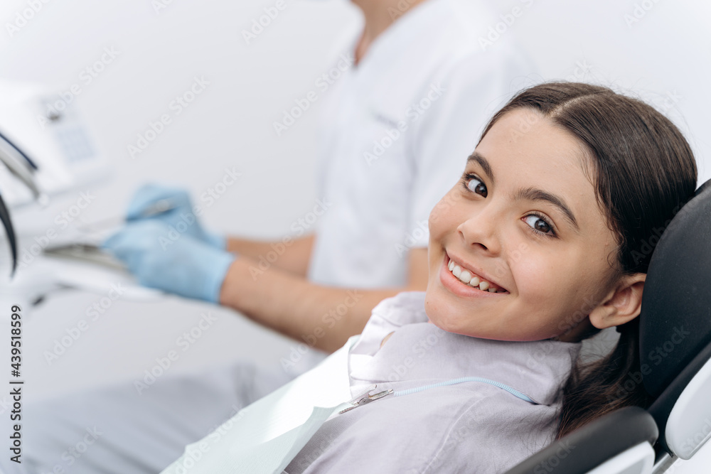 Attractive girl sitting in a dental chair, looking at the camera. Beautiful little girl smiling Attractive girl sitting in a dental chair, looking at the camera. Beautiful little girl smiling