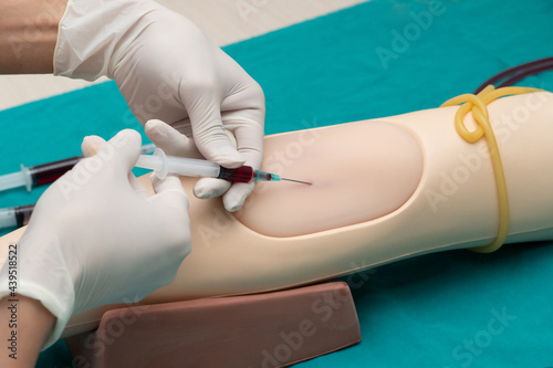 Canvas Print Doctor or nurse hands in medical white gloves using needle syringe drawing blood sample from manikin arm in hospital