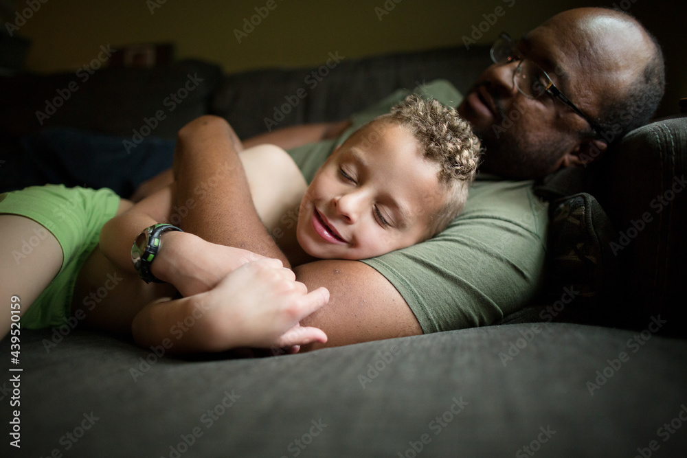 Boy snuggles with father on couch Boy snuggles with father on couch