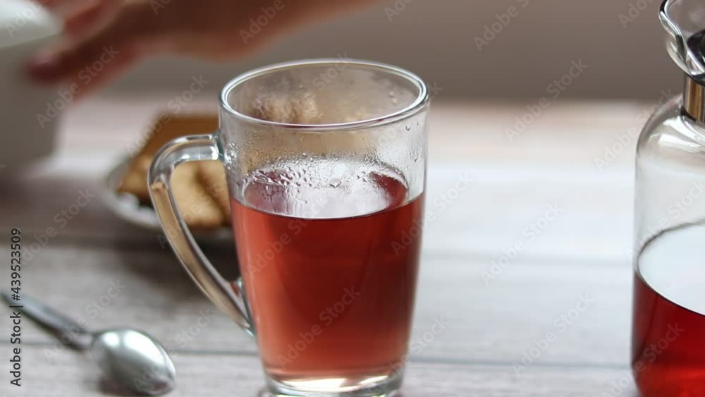 Pouring fruit tea into a transparent cup. In the background are cookies and a sugar bowl. Pouring fruit tea into a transparent cup. In the background are cookies and a sugar bowl.