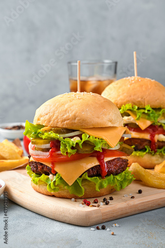 Burgers with meat, cheese and vegetables on the background of cola and French fries.