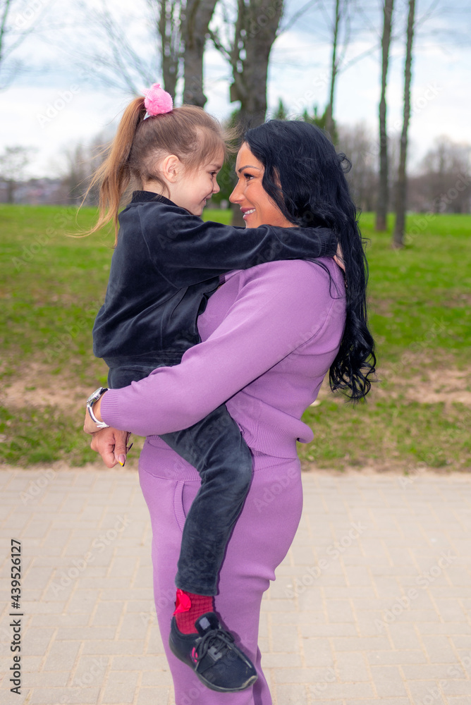 Beautiful mother and daughter play hugs in a summer park nature in profile looking at each other.