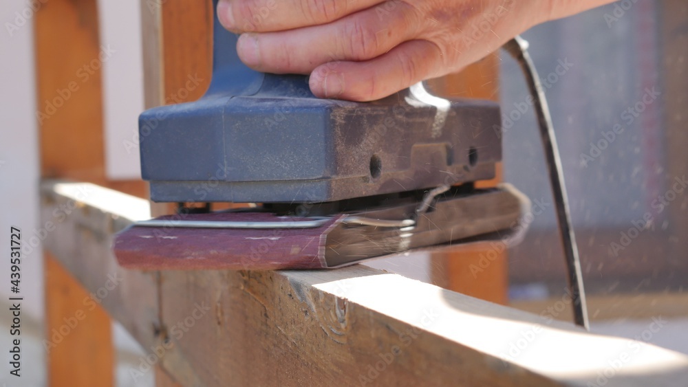 hand of carpenter using electric wood sander with sandpaper sanding a wooden