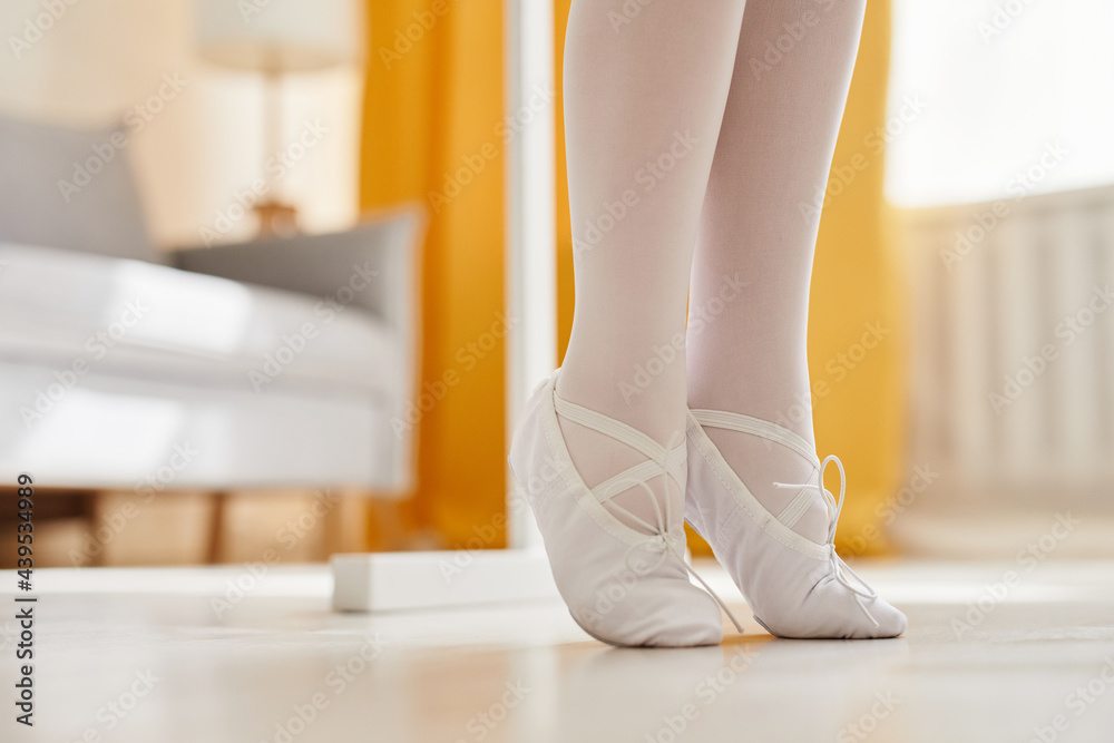 Close up of tiny ballerina feet standing on tip toes in home interior lit by sunlight, copy space