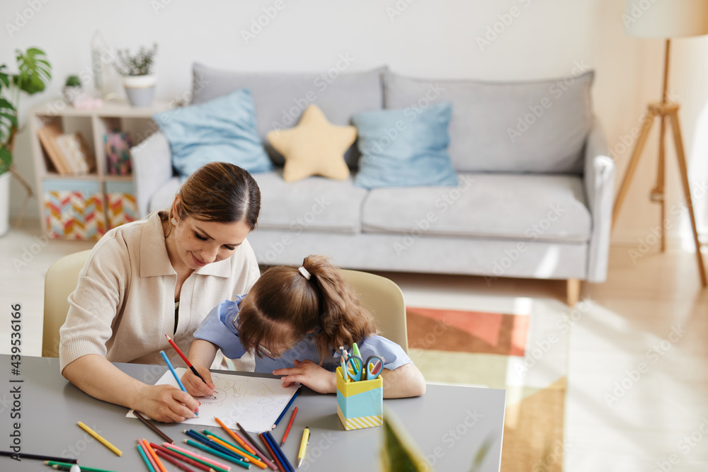 High angle portrait of cute girl with down syndrome studying at home with mother helping her in cozy interior, copy space