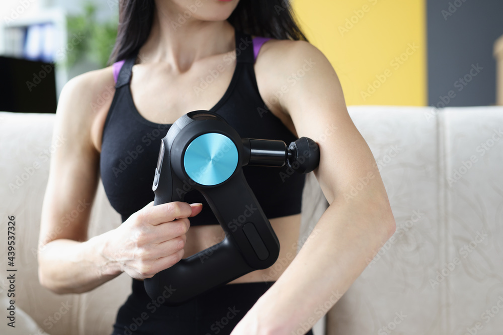 Young woman doing massage with percussion massager at home
