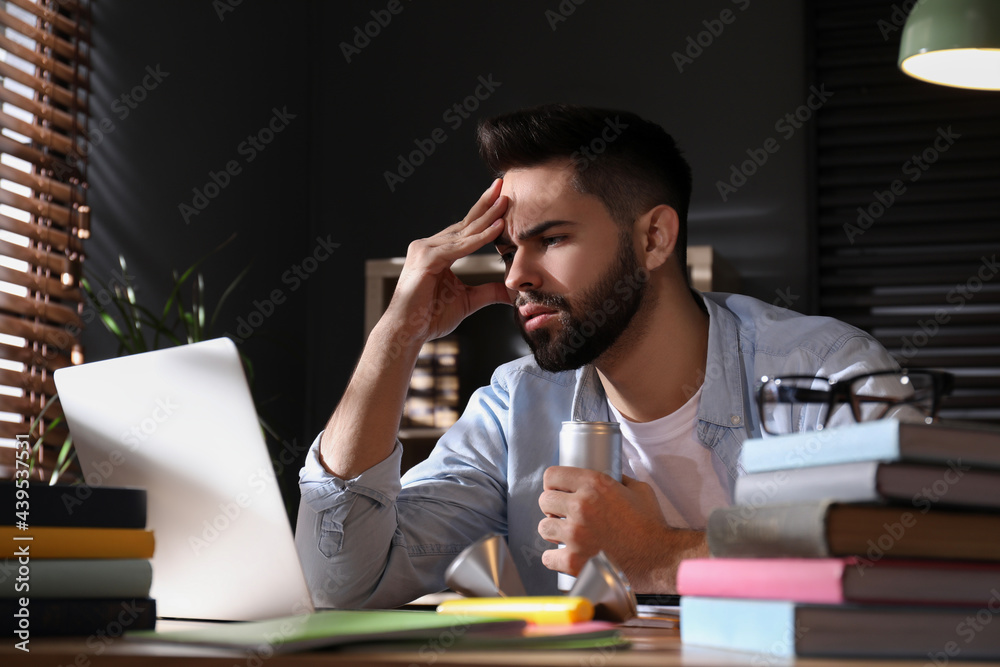 Obraz premium Tired young man with energy drink studying at home