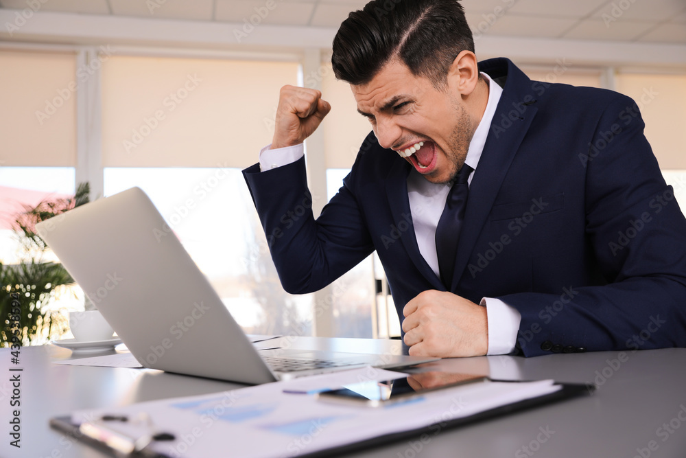 Emotional businessman with laptop at table in office Emotional businessman with laptop at table in office