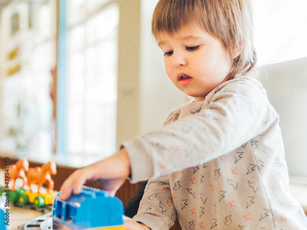 Toddler plays with colorful toy blocks. Little boy stares on figure from toy constructor. Interior of kindergarten or nursery. Indoors leisure activity for children. Toddler plays with colorful toy blocks. Little boy stares on figure from toy constructor. Interior of kindergarten or nursery. Indoors leisure activity for children.
