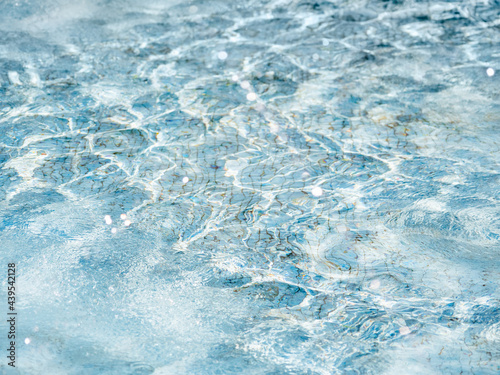 Sun beams on surface of water in swimming pool or fountain with blue mosaic bottom. Abstract background with wavy pattern of clear transparent water.