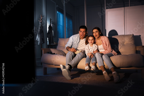 Family watching movie with popcorn on sofa at night