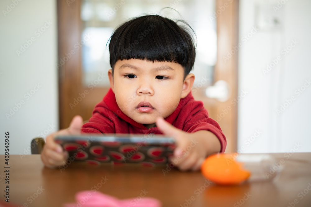 Asian kid watching smartphone on Dining table Asian kid watching smartphone on Dining table