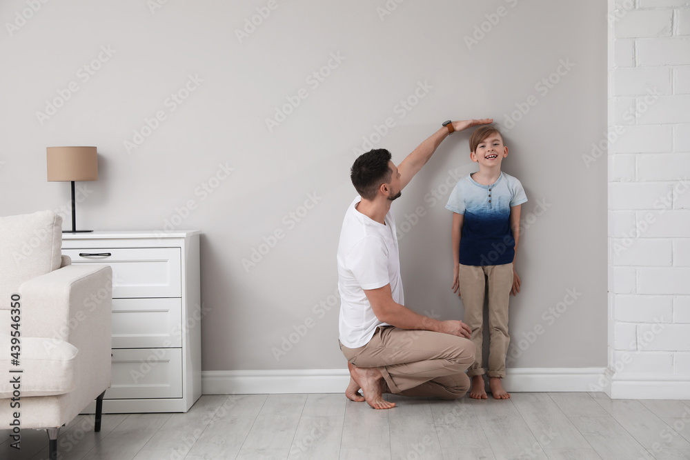 Father measuring height of his son near wall at home Father measuring height of his son near wall at home