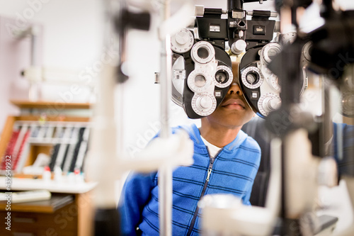 Boy peers through phoropter at optometrist photo