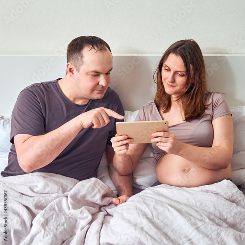 A smiling man and a pregnant woman watch training on a tablet over the Internet © Андрей Журавлев