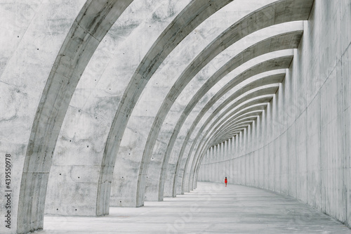A girl dressed in red walks through concrete arches. photo