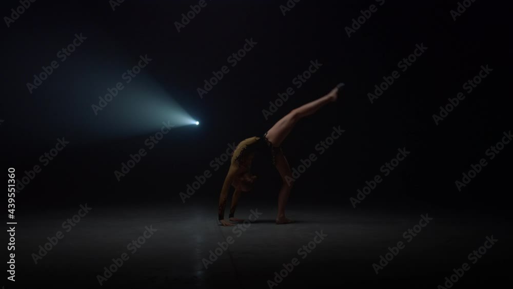 Flexible girl doing somersault in dark space in dark space. Sportswoman tumbling