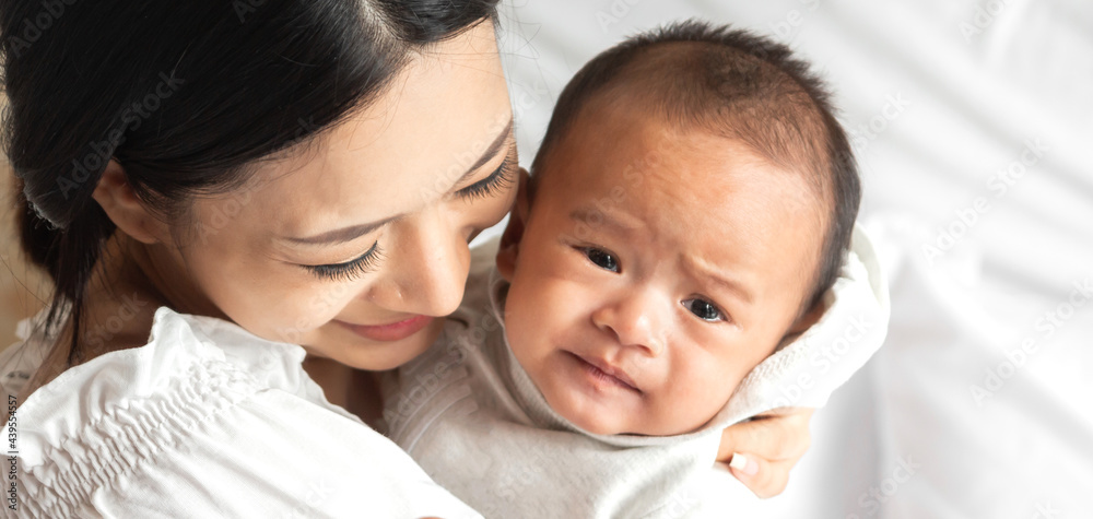 Portrait of enjoy happy love family asian mother playing with adorable little asian baby.Mom kiss with cute son moments good time in a white bedroom.Love of family concept