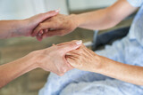 Hände von Pflegerin halten Hände von einer Seniorin