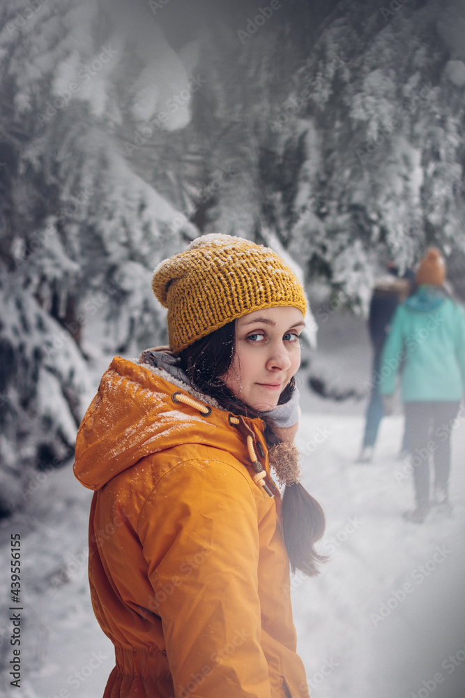 young brunette dressed in an orange jacket looks with a nice realistic smile at her boyfriend and waits for him. Winter relax. A walk in the wild nature