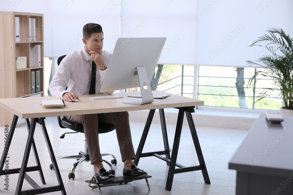 Man using footrest while working on computer in office - obrazy, fototapety, plakaty 