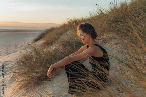 Woman sitting in the sand dunes at the beach during sunset photo