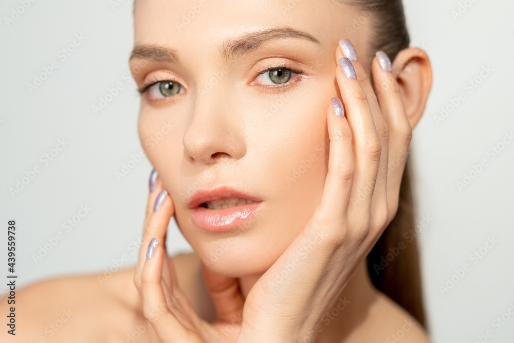 Skin care. Facial treatment. Freshness wellness. Confident woman with nude makeup touching radiant clean smooth face isolated on light neutral background.