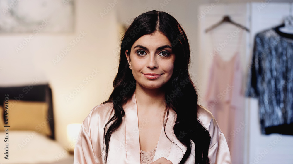 cheerful brunette young woman in pink peignoir with long hair looking at camera in bedroom cheerful brunette young woman in pink peignoir with long hair looking at camera in bedroom