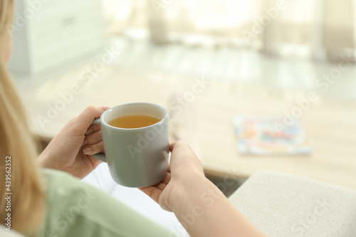 Young woman with cup of hot tea relaxing at home, closeup