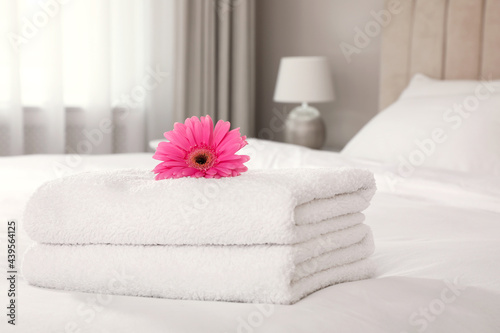 Stack of fresh towels with flower on bed indoors