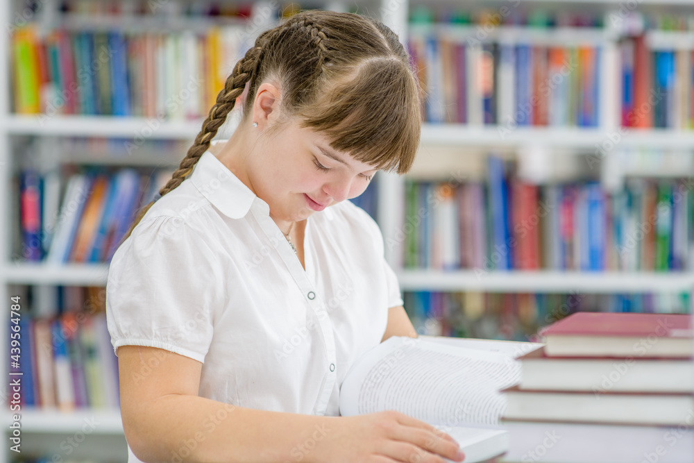 Clever girl with syndrome down reads a book at library. Education for disabled children concept Clever girl with syndrome down reads a book at library. Education for disabled children concept