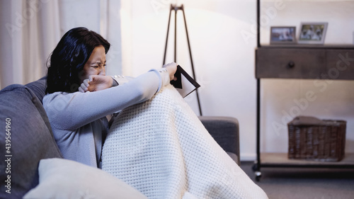 Foto crying woman sitting on sofa, holding envelope and covering face with hand at ho