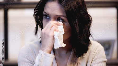 crying brunette woman wiping tears with paper napkin at home