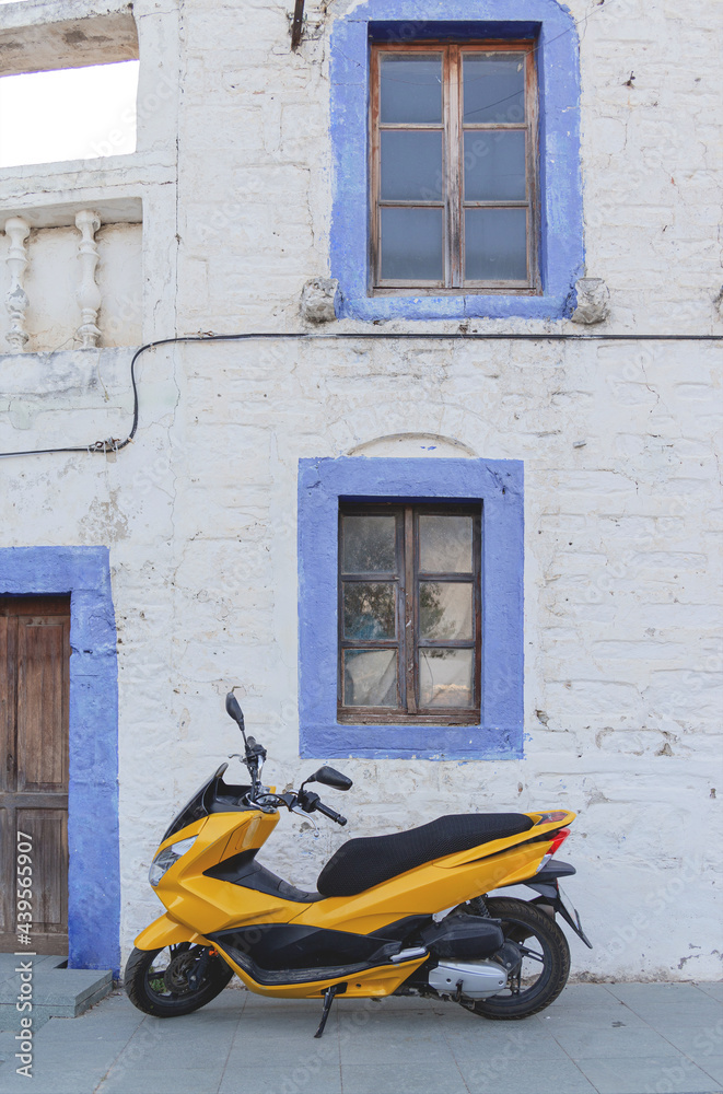 Yellow motorcycle near white building with blue window frames in the Greek style. Travel and architecture concept. Bodrum, Turkey