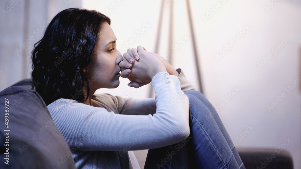 upset woman sitting on sofa and holding clenched hands near face at home upset woman sitting on sofa and holding clenched hands near face at home
