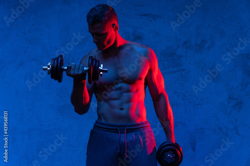 Muscular bodybuilder man exercising with dumbbells in colorful neon light