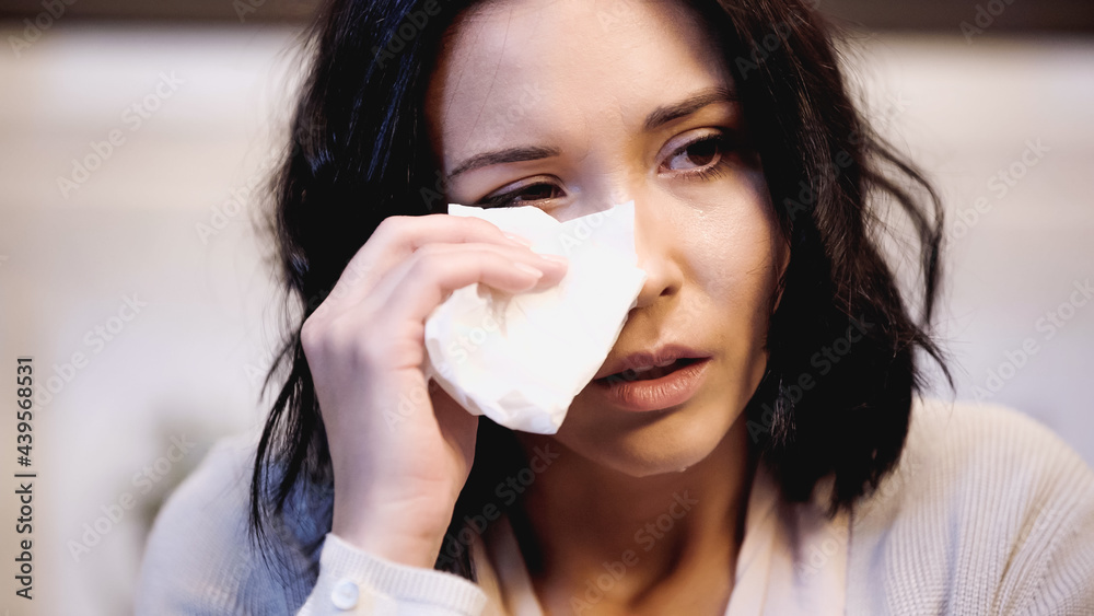 portrait of crying brunette woman wiping tears with white paper napkin at home portrait of crying brunette woman wiping tears with white paper napkin at home