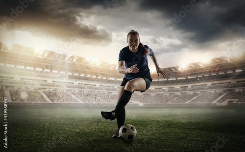Female soccer, football player dribbling ball in motion at the stadium during sport match on cloudy sky background. Collage © master1305