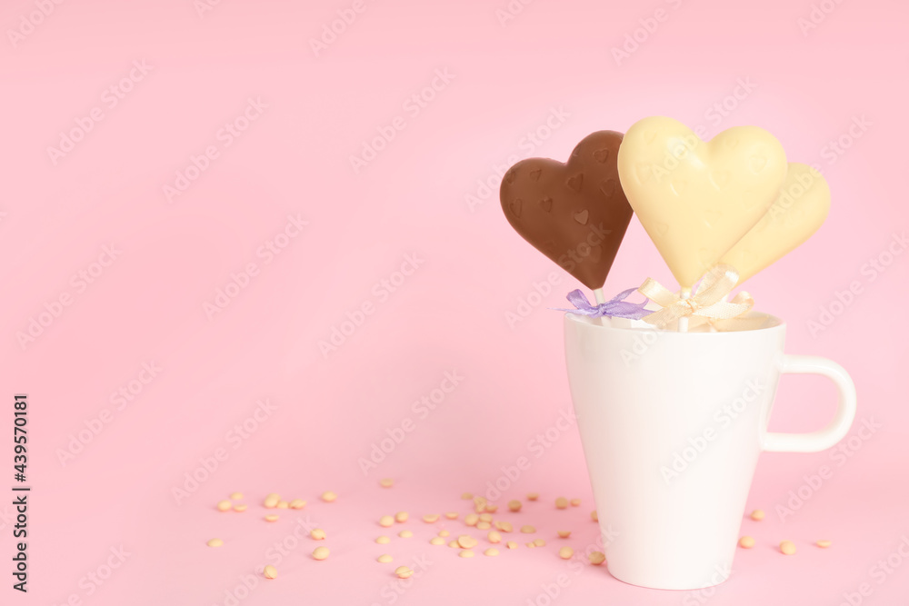 Different chocolate heart shaped lollipops in cup on light pink background. Space for text Different chocolate heart shaped lollipops in cup on light pink background. Space for text