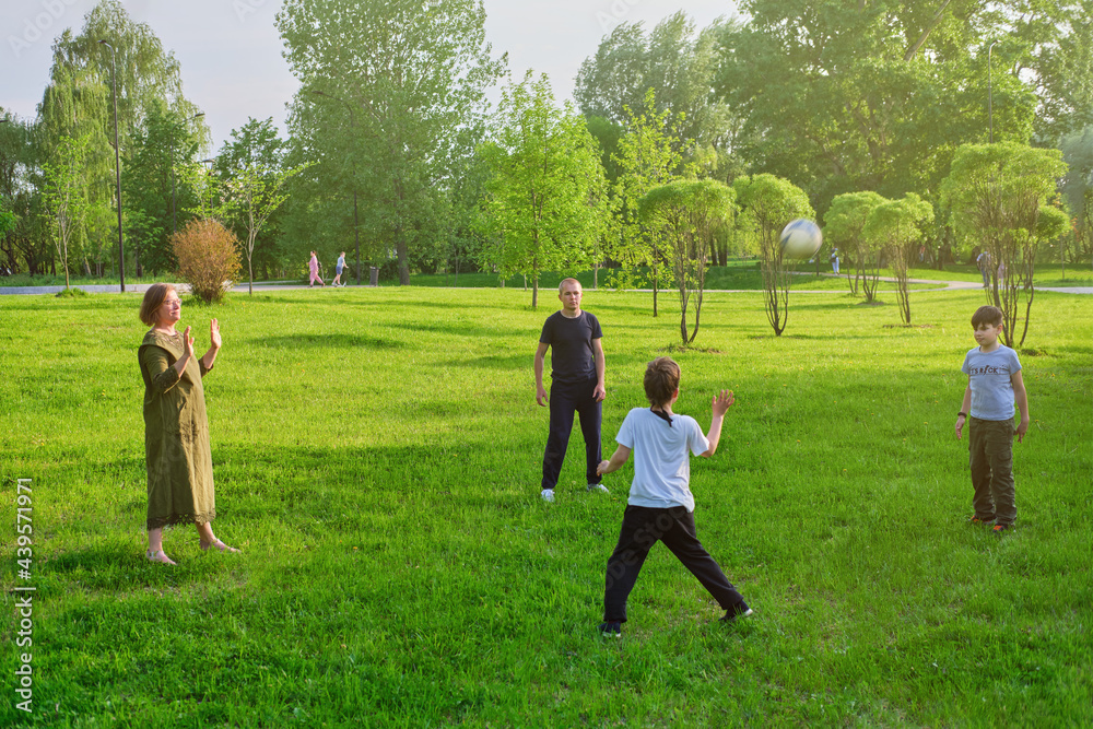 Mom, dad and sons play sports with a soccer ball on the park lawn