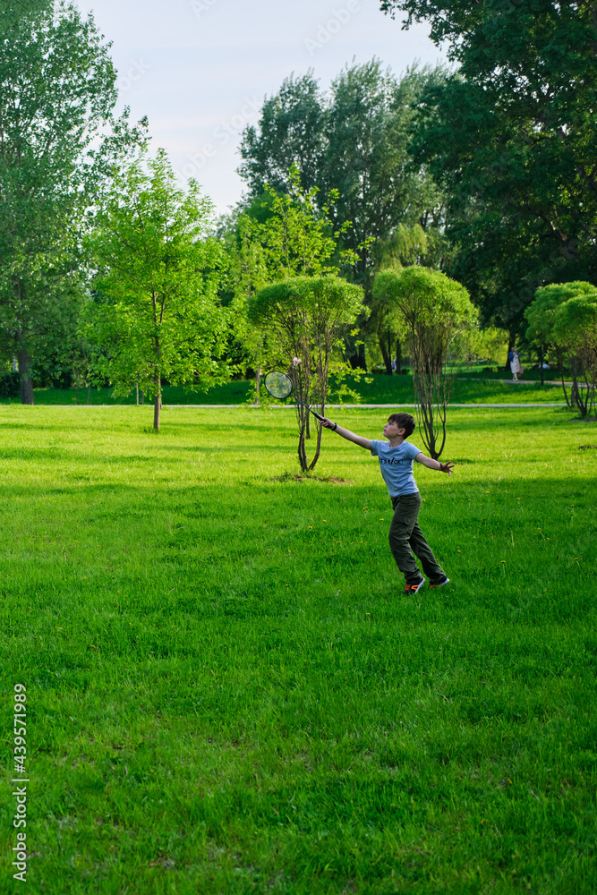 A boy plays badminton during outdoor recreation, lawn in the park A boy plays badminton during outdoor recreation, lawn in the park