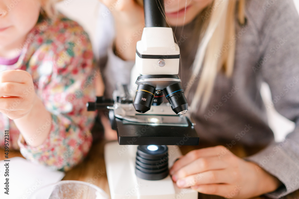 young girl and little sister looking through microscope young girl and little sister looking through microscope