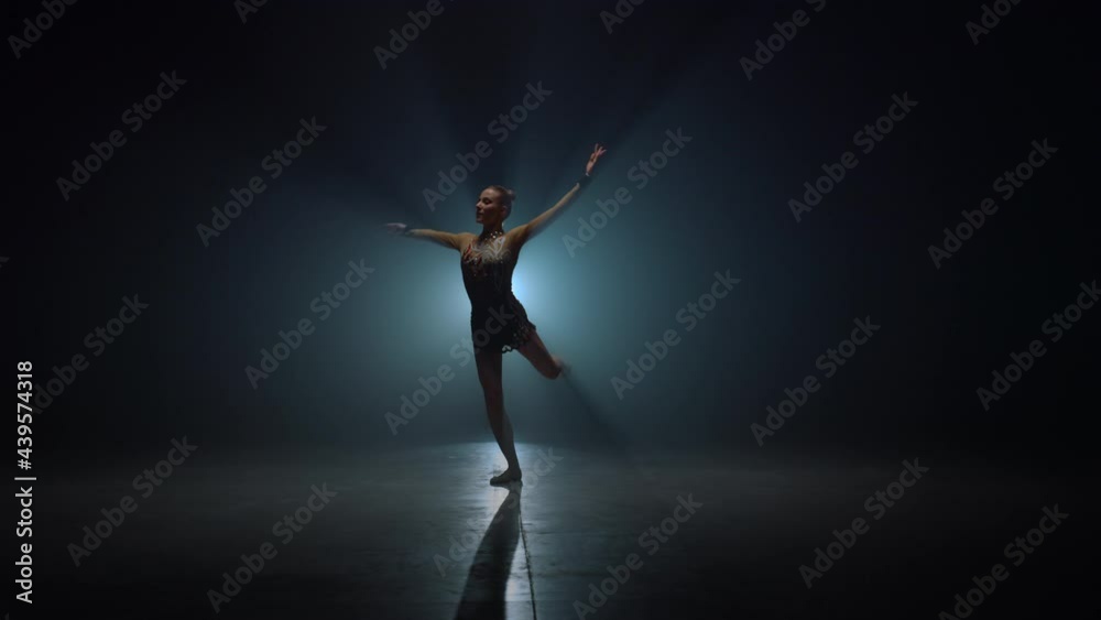 Graceful gymnast spinning around indoors. Slim woman dancing in dark space. Graceful gymnast spinning around indoors. Slim woman dancing in dark space.