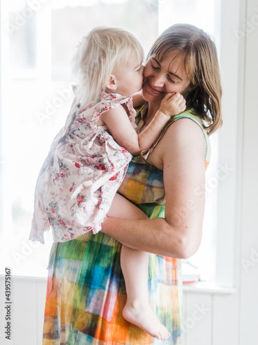 Daughter sits on pregnant belly and kisses mum photo