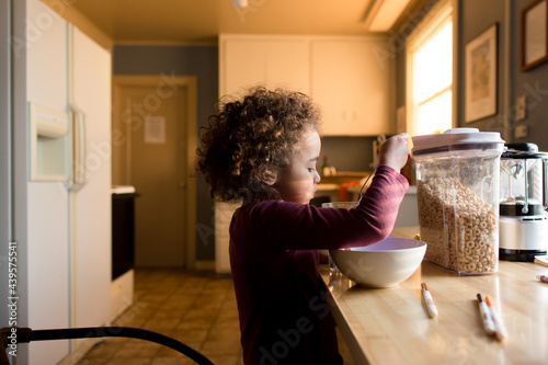 Girl eats cereal in sunlit kitchen
