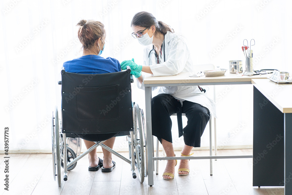 Elderly, senior woman wearing a mask to sit in a wheelchair, a nurse or a doctor wearing a mask, vaccinating a patient in a hospital to prevent COVID-19 