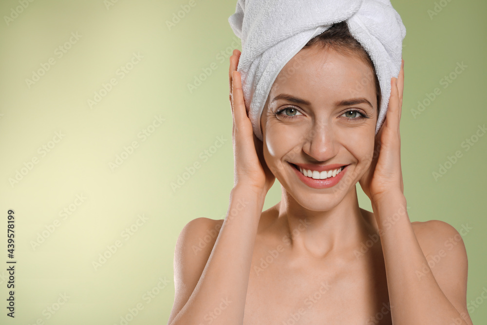 Beautiful young woman with hair wrapped in towel after washing on light green background. Space for text