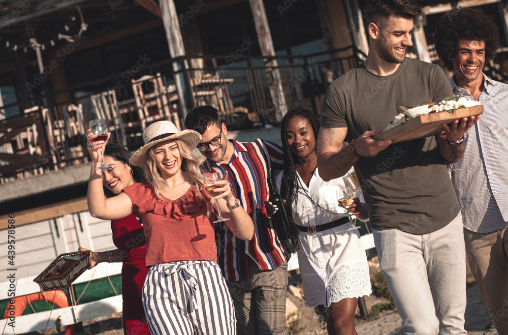 Obraz premium Diverse group of friends carry food and wine to the outdoor dinner table.